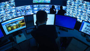 Control room operator sitting at a desk with multiple screens, beyond which is a large video wall